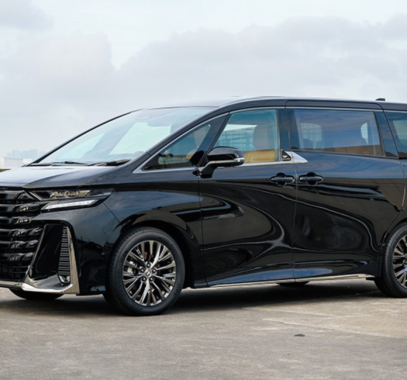 A sleek, black luxury 7-seater MPV parked in an open-air lot in Singapore.